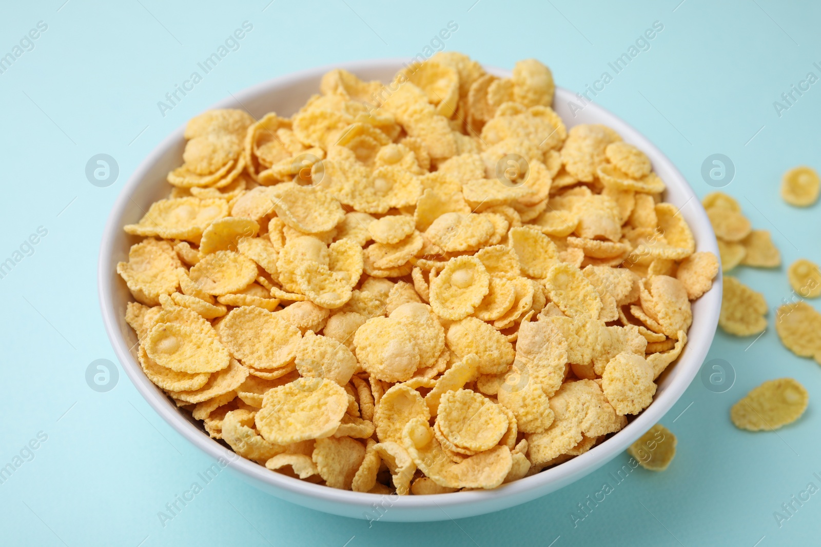 Photo of Breakfast cereal. Tasty corn flakes in bowl on light blue table, closeup