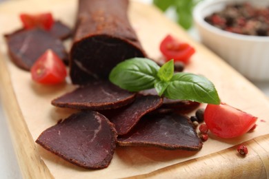 Photo of Delicious dry-cured beef basturma with basil and tomatoes on table, closeup