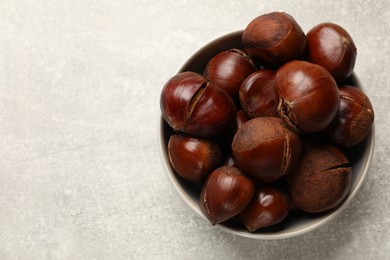 Photo of Fresh edible sweet chestnuts in bowl on grey table, top view. Space for text