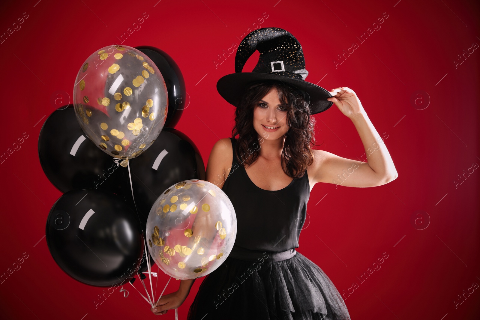 Photo of Beautiful woman in witch costume with balloons on red background. Halloween party