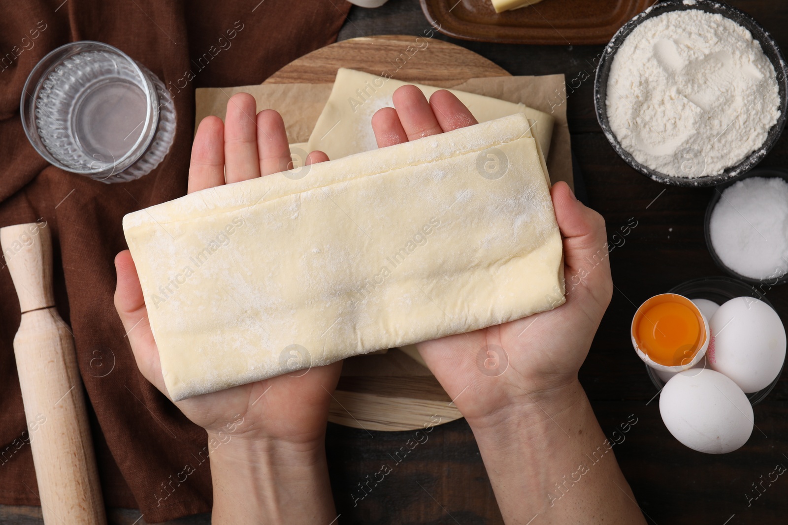 Photo of Man holding raw puff pastry dough at wooden table, top view