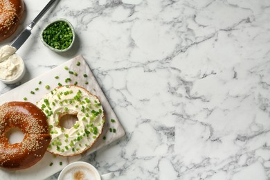 Delicious bagel with cream cheese and green onion on white marble table, flat lay. Space for text