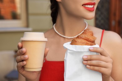 Photo of Woman with croissant and paper cup of coffee outdoors, closeup