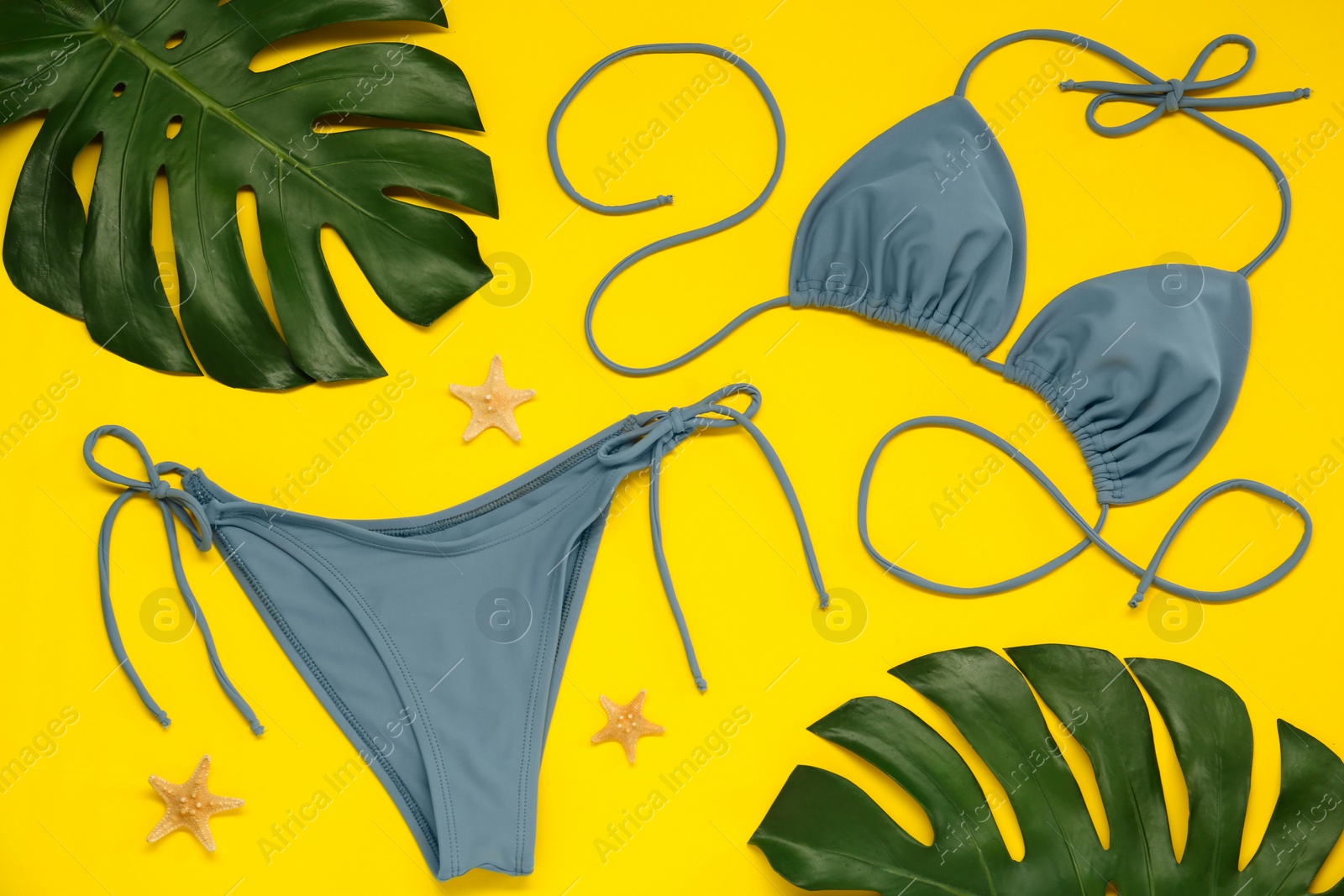 Photo of Stylish blue bikini, leaves and starfishes on yellow background, flat lay