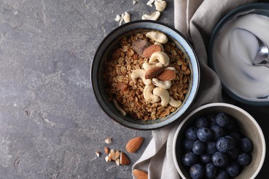 Photo of Tasty granola in bowl, blueberries and yogurt on gray textured table, flat lay. Space for text
