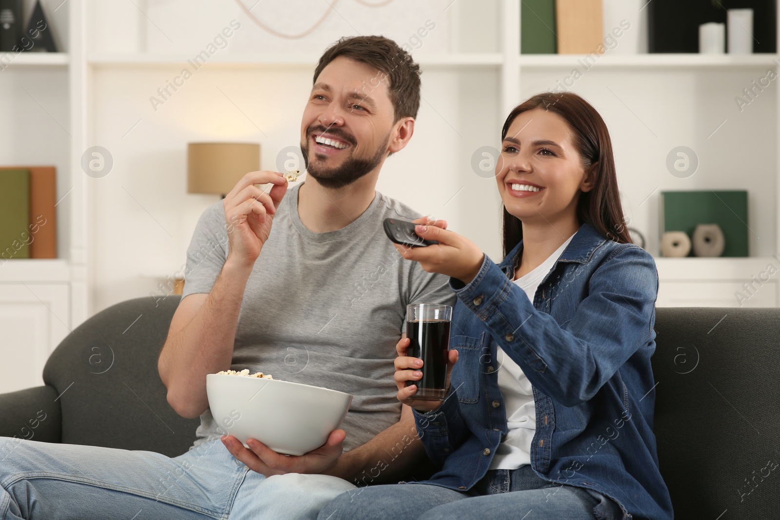 Photo of Happy couple watching show at home. Woman changing TV channels with remote control