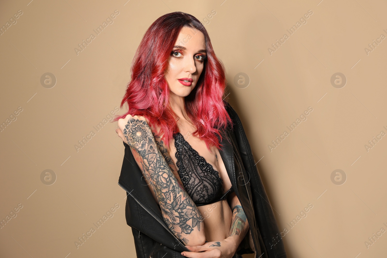 Photo of Beautiful woman with tattoos on arms against beige background