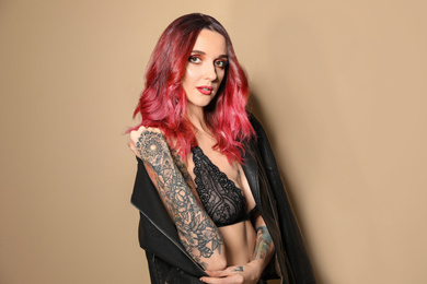 Beautiful woman with tattoos on arms against beige background