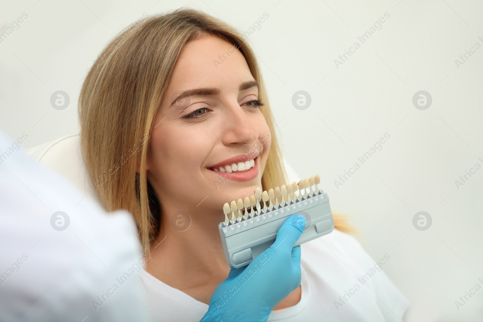 Photo of Doctor matching patient's teeth color with palette on light background, closeup. Cosmetic dentistry