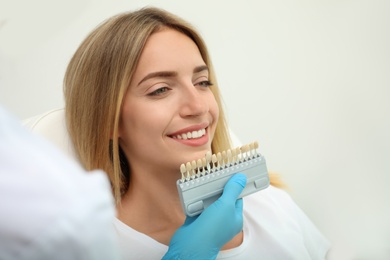 Doctor matching patient's teeth color with palette on light background, closeup. Cosmetic dentistry