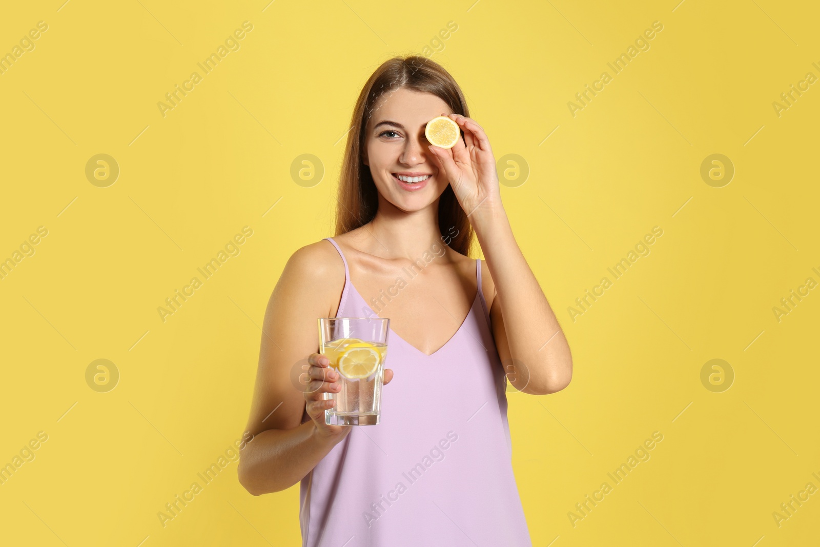 Photo of Young woman with glass of lemon water on yellow background