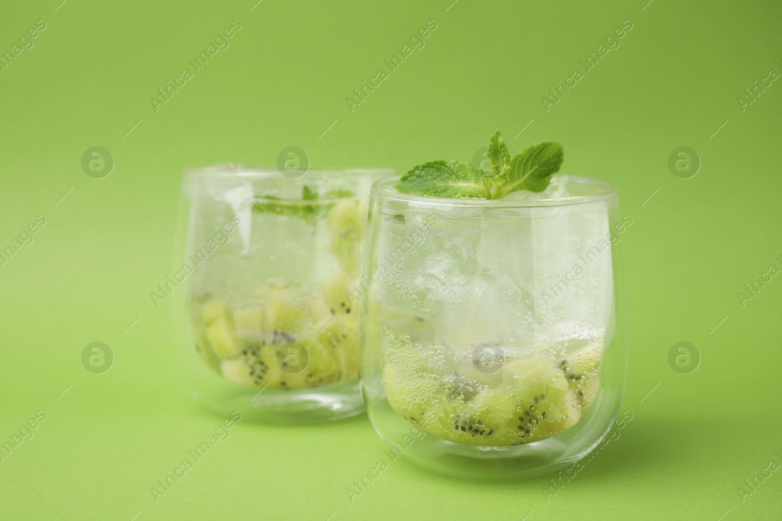 Photo of Glasses of refreshing drink with kiwi and mint on light green background, closeup