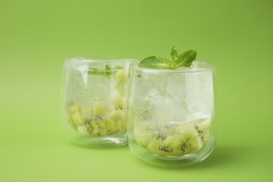 Glasses of refreshing drink with kiwi and mint on light green background, closeup