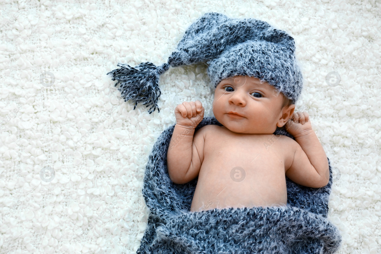 Photo of Cute little baby in grey hat and plaid lying on soft blanket, top view. Space for text