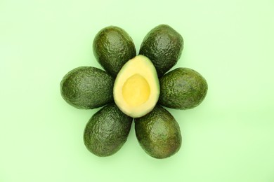 Tasty whole and cut avocados on light green background, flat lay