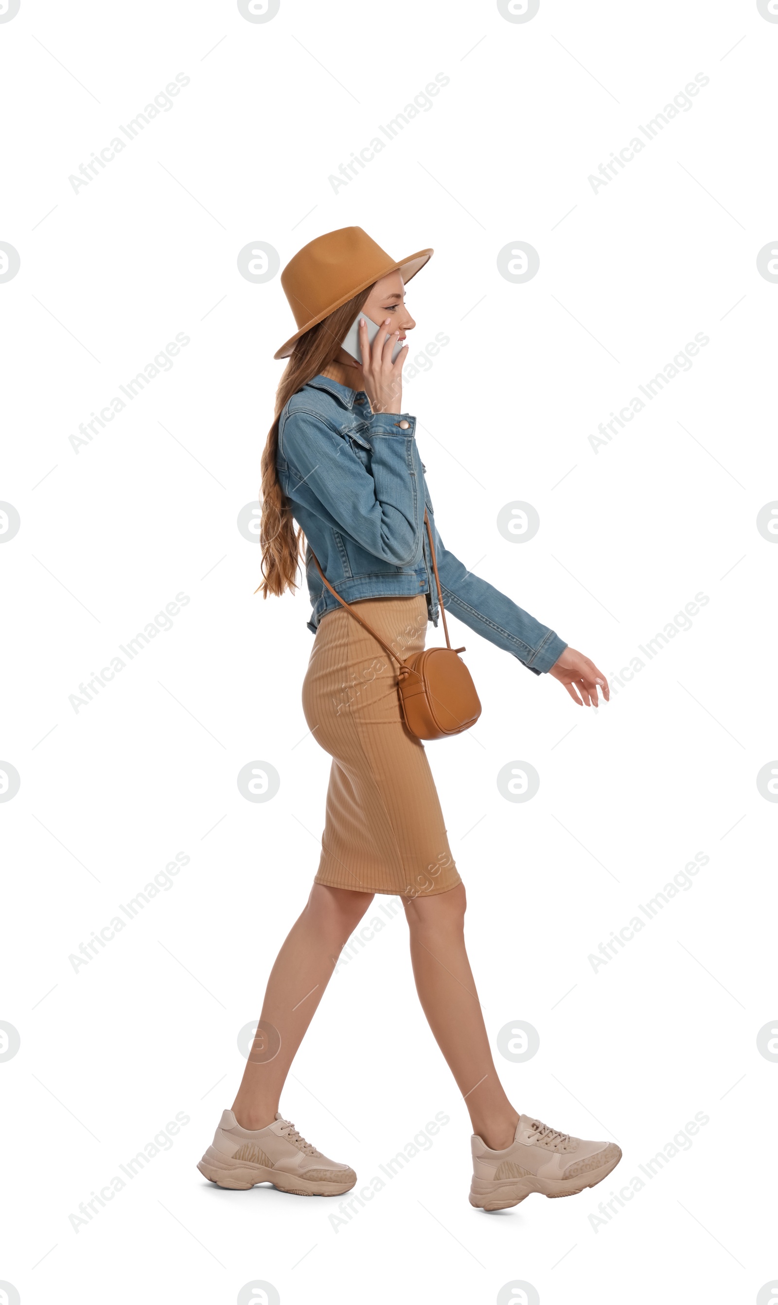 Photo of Young woman in casual outfit talking on smartphone while walking against white background