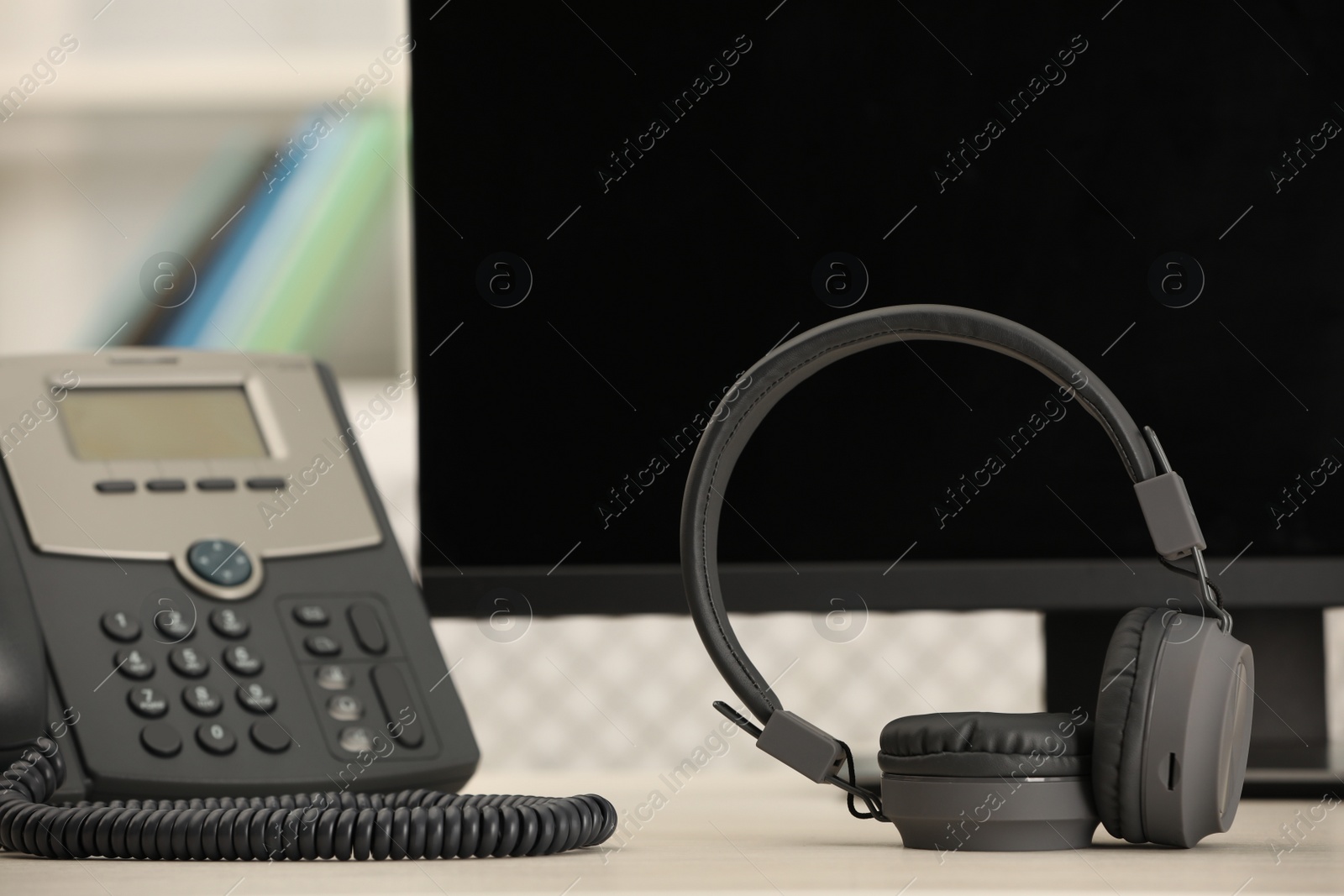 Photo of Modern headphones, desktop telephone and computer on table indoors