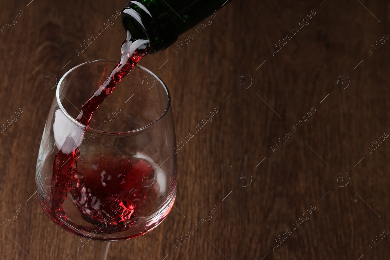 Photo of Pouring tasty red wine in glass at wooden table, closeup. Space for text