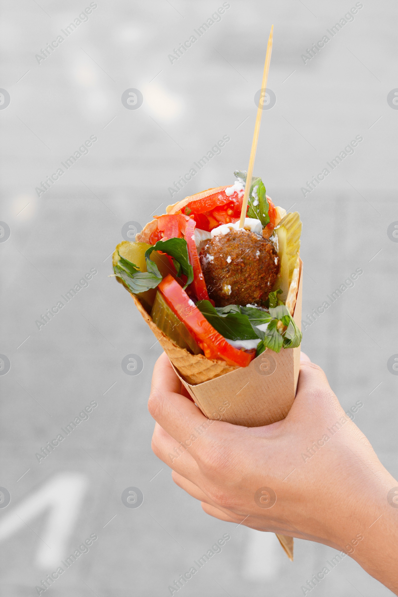 Photo of Woman holding wafer with falafel and vegetables outdoors, closeup. Street food