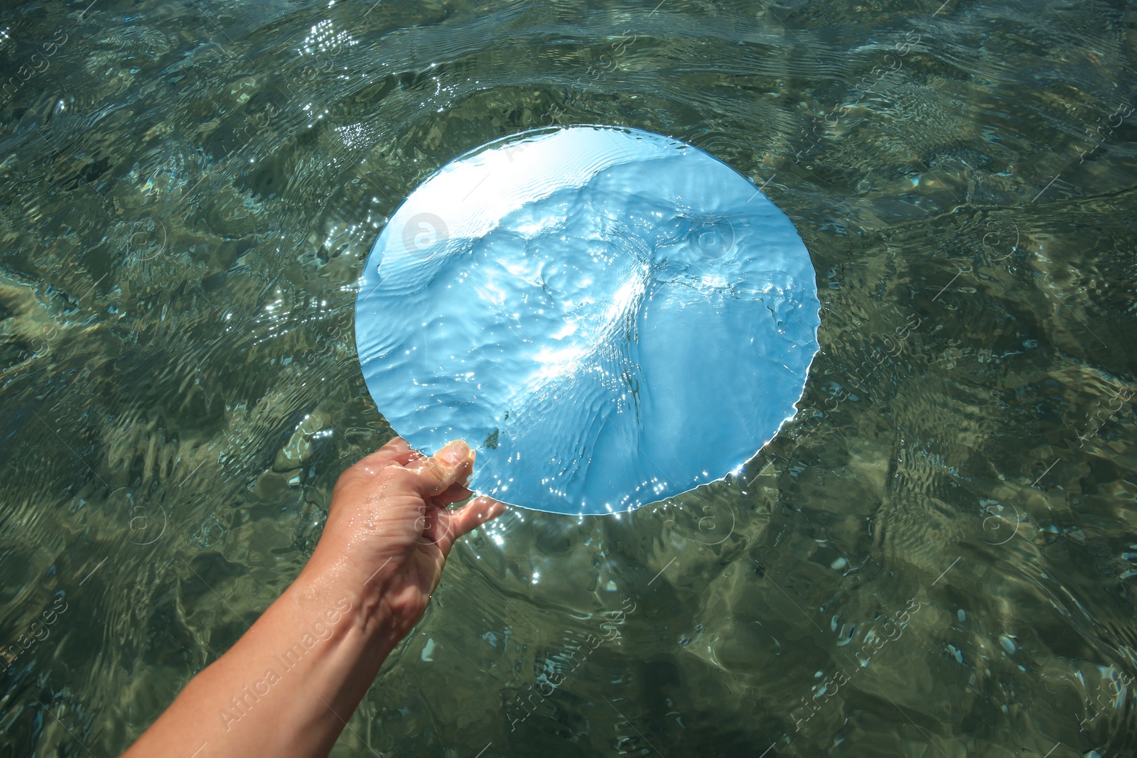 Photo of Woman immersing round mirror in sea on sunny day, above view