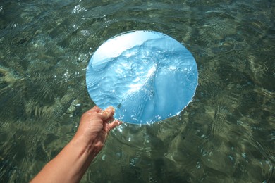 Photo of Woman immersing round mirror in sea on sunny day, above view