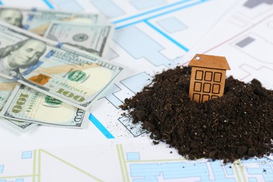 Photo of Money and small house model in pile of soil on cadastral maps