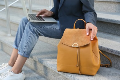 Photo of Young woman with stylish backpack working on laptop outdoors, closeup