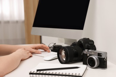 Photo of Photographer working on computer at white table with cameras indoors, closeup