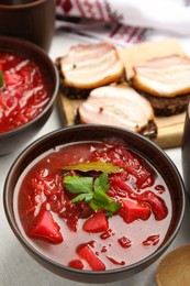 Photo of Stylish brown clay bowl with Ukrainian borsch served on white tablecloth