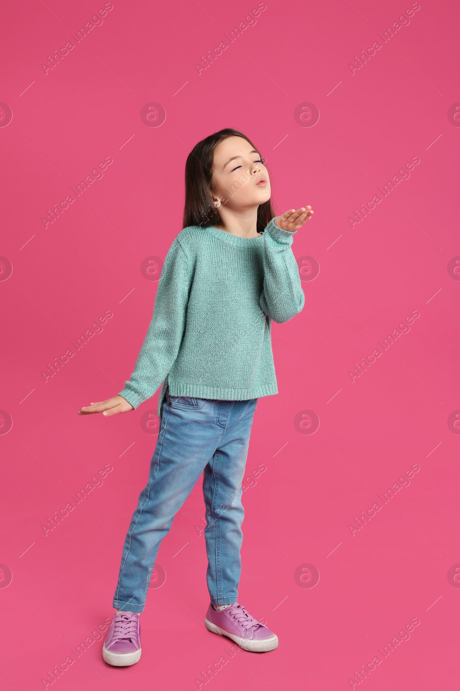Photo of Cute little girl blowing air kiss on pink background