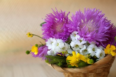 Bouquet of beautiful wildflowers in wicker basket on beige background, closeup. Space for text
