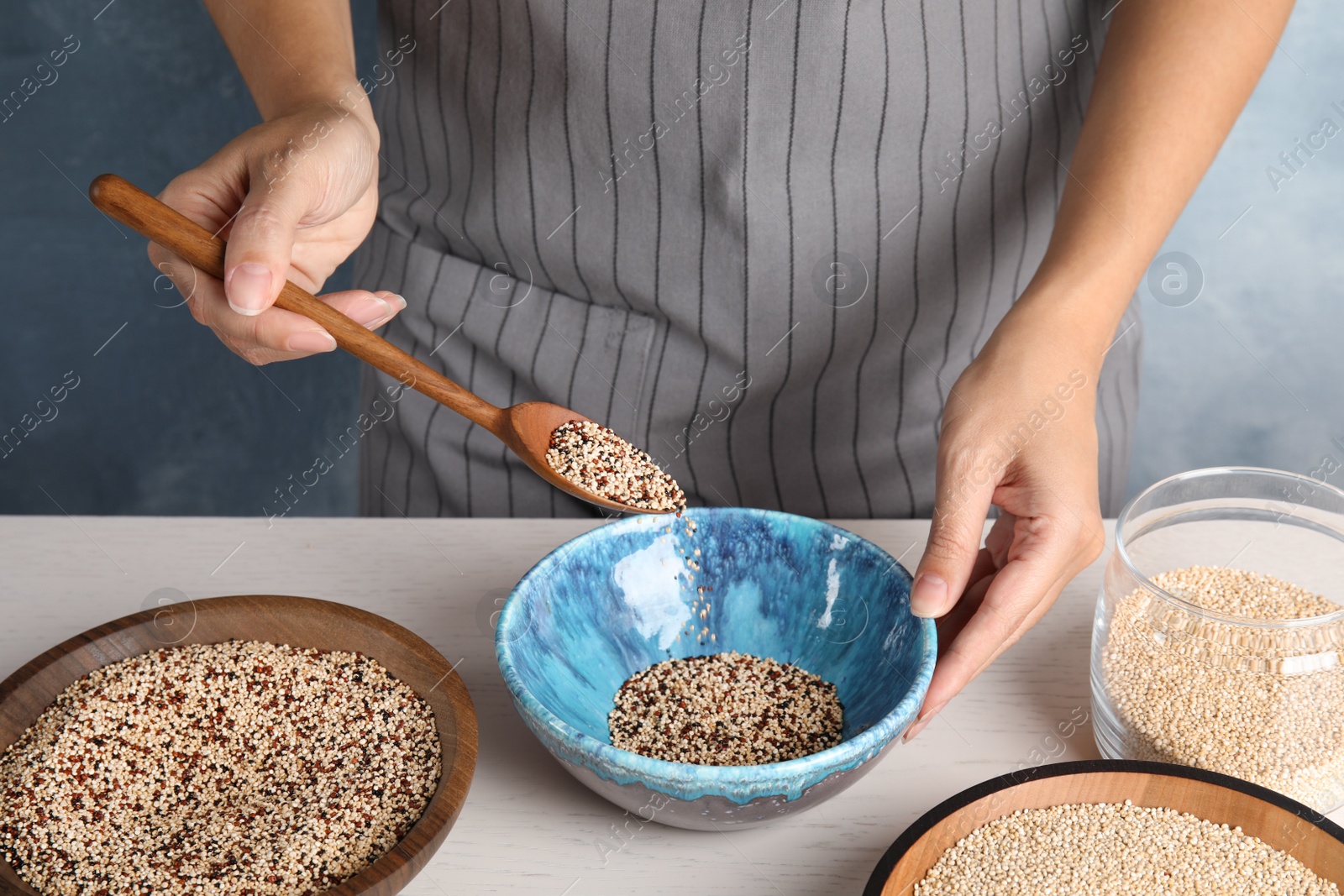 Photo of Woman pouring mixed quinoa seeds into bowl at table, closeup