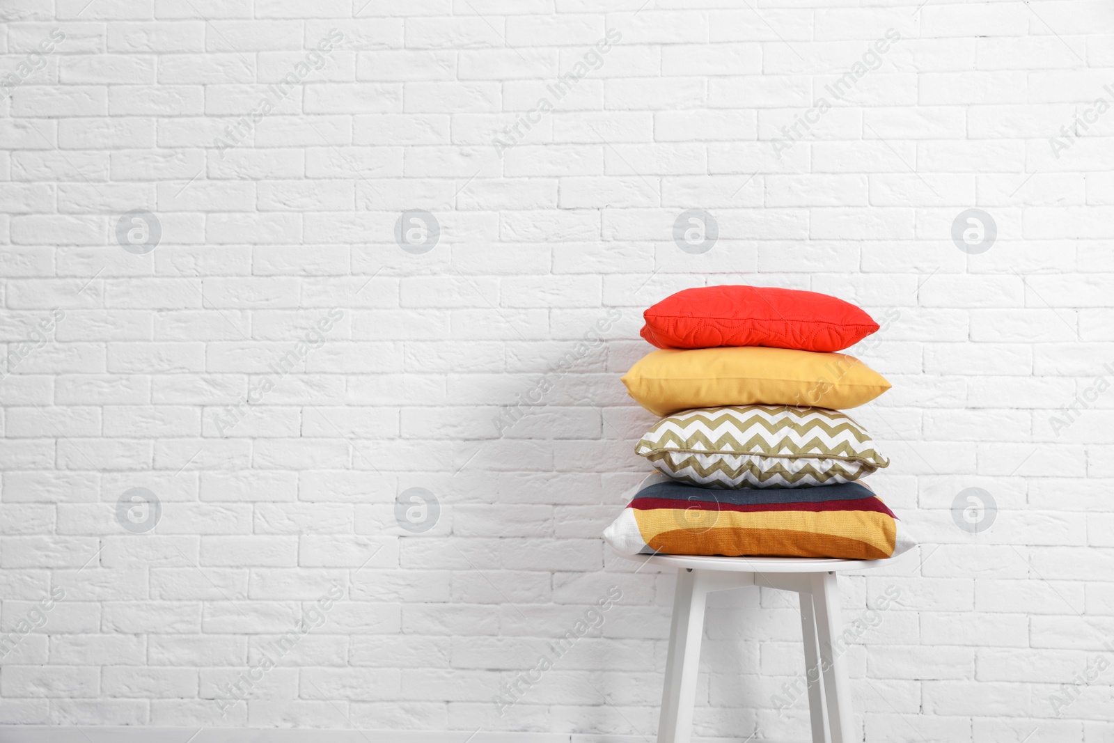 Photo of Many different pillows on chair near brick wall with space for text