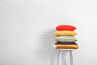 Photo of Many different pillows on chair near brick wall with space for text