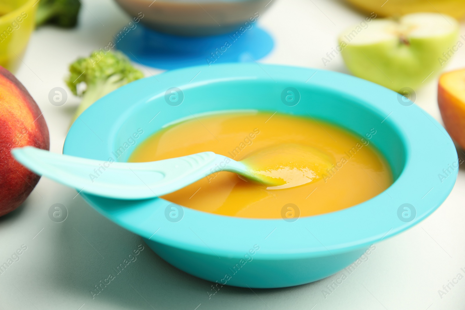 Photo of Baby food in bowl and fresh ingredients on white table, closeup