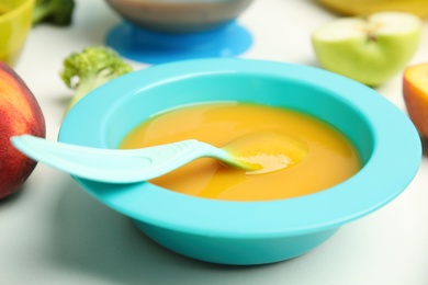 Baby food in bowl and fresh ingredients on white table, closeup