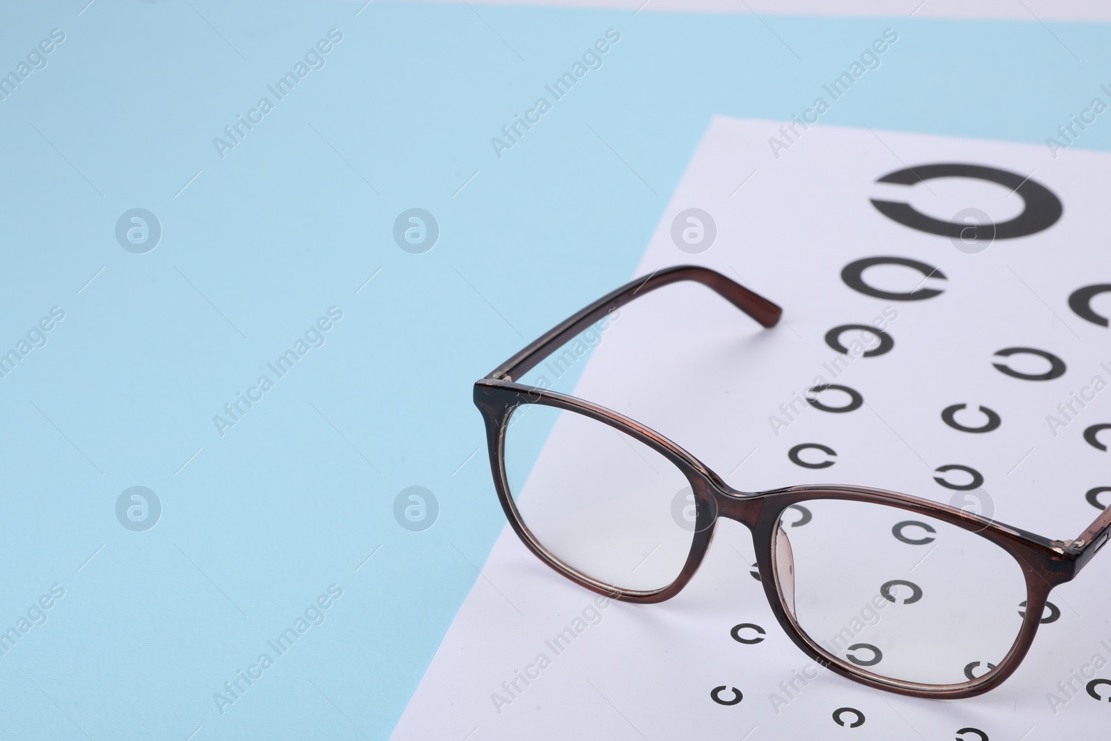 Photo of Vision test chart and glasses on light blue background, space for text