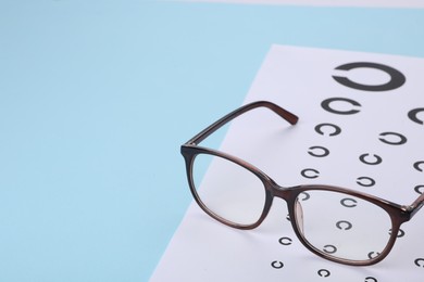 Vision test chart and glasses on light blue background, space for text