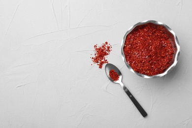 Photo of Bowl and spoon with chili pepper flakes on light background, top view