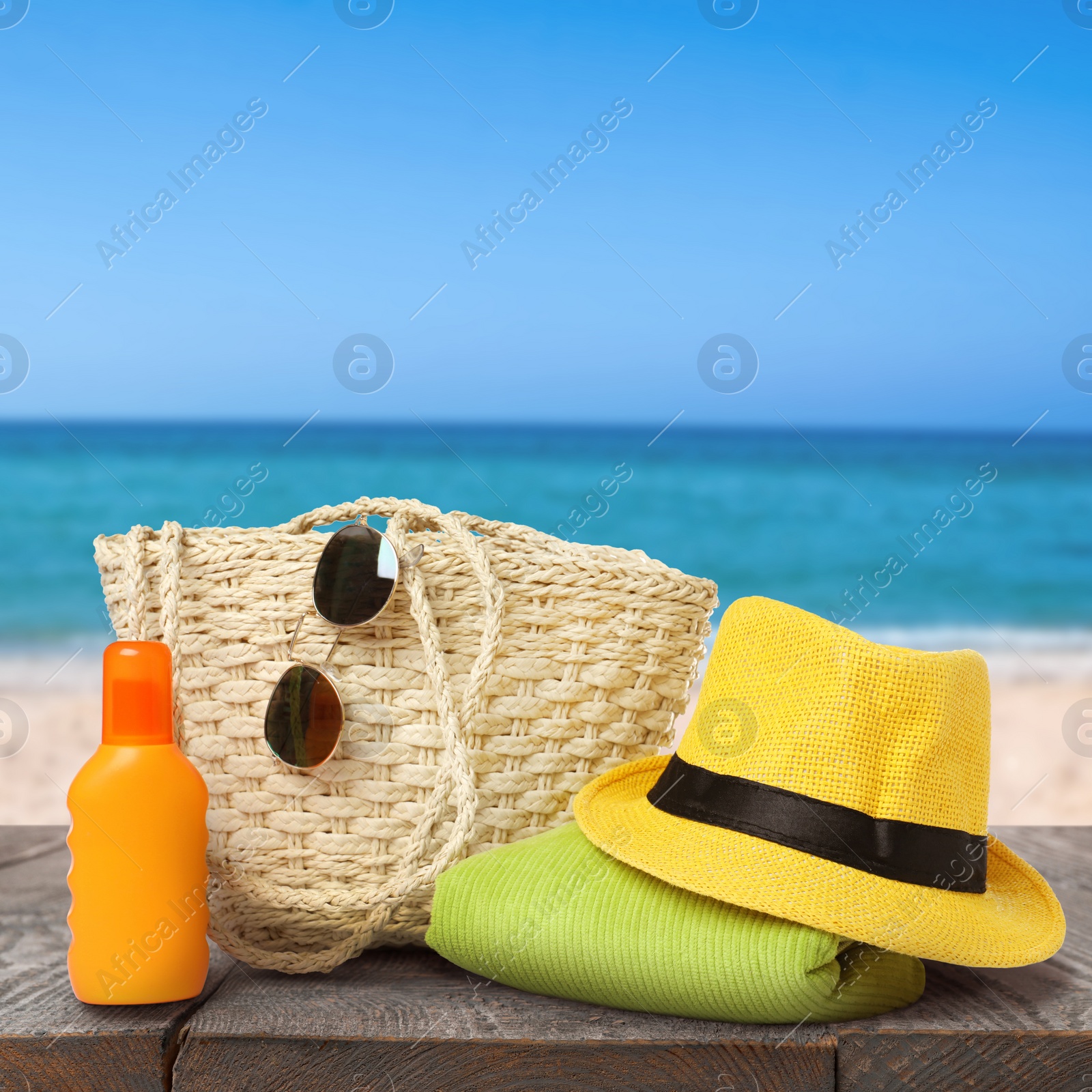 Image of Stylish bag with beach accessories on wooden surface near seashore 