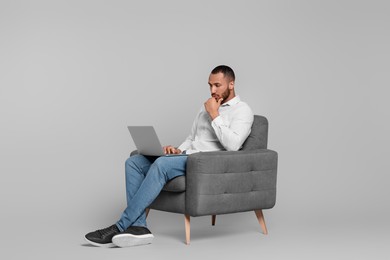 Photo of Thoughtful young man with laptop sitting in armchair on grey background