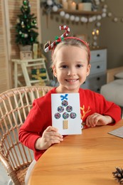 Cute little child with beautiful Christmas greeting card at home