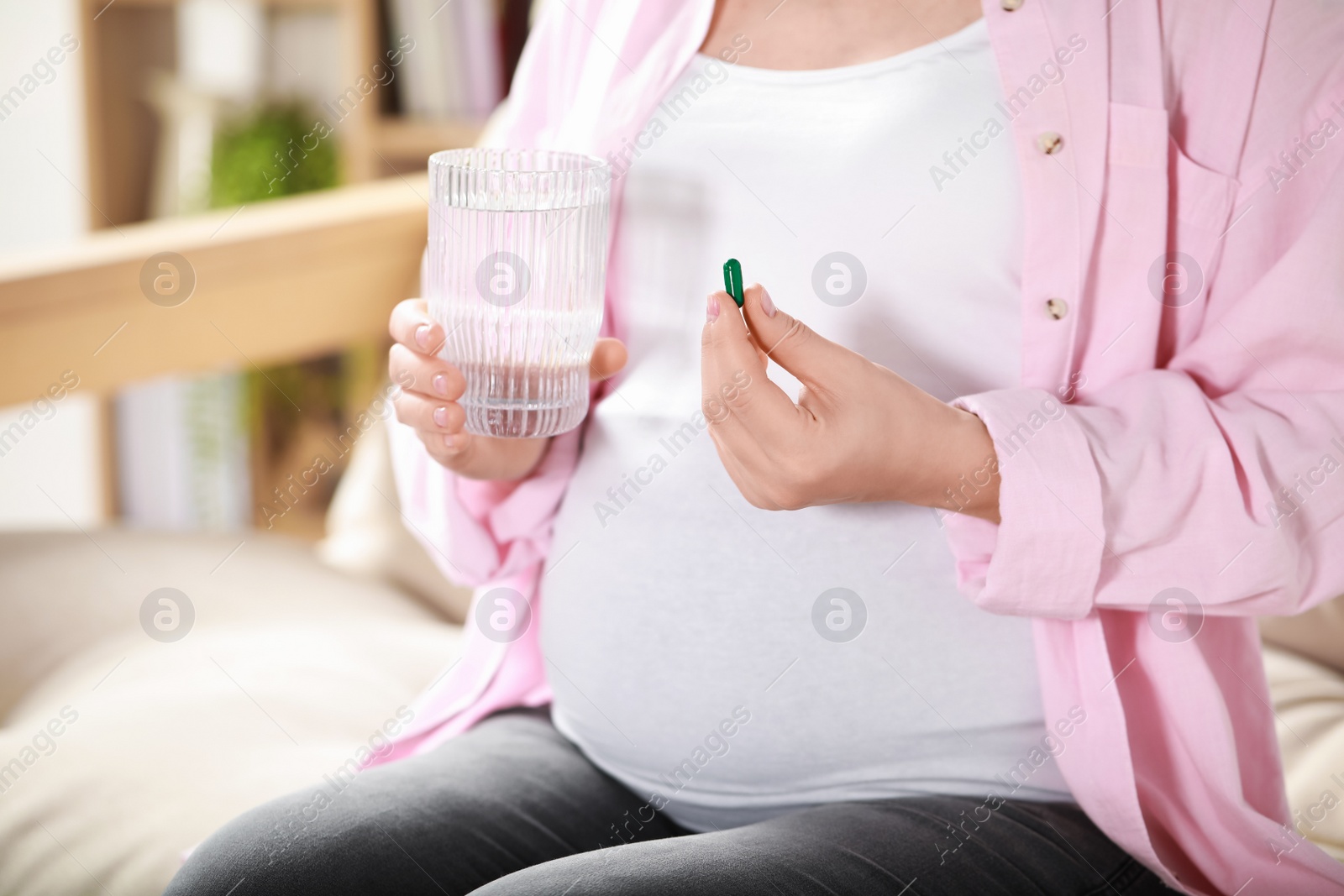 Photo of Pregnant woman holding pill and glass of water at home, closeup