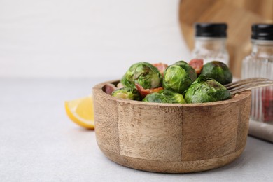 Photo of Delicious roasted Brussels sprouts and bacon in bowl on light table, closeup. Space for text