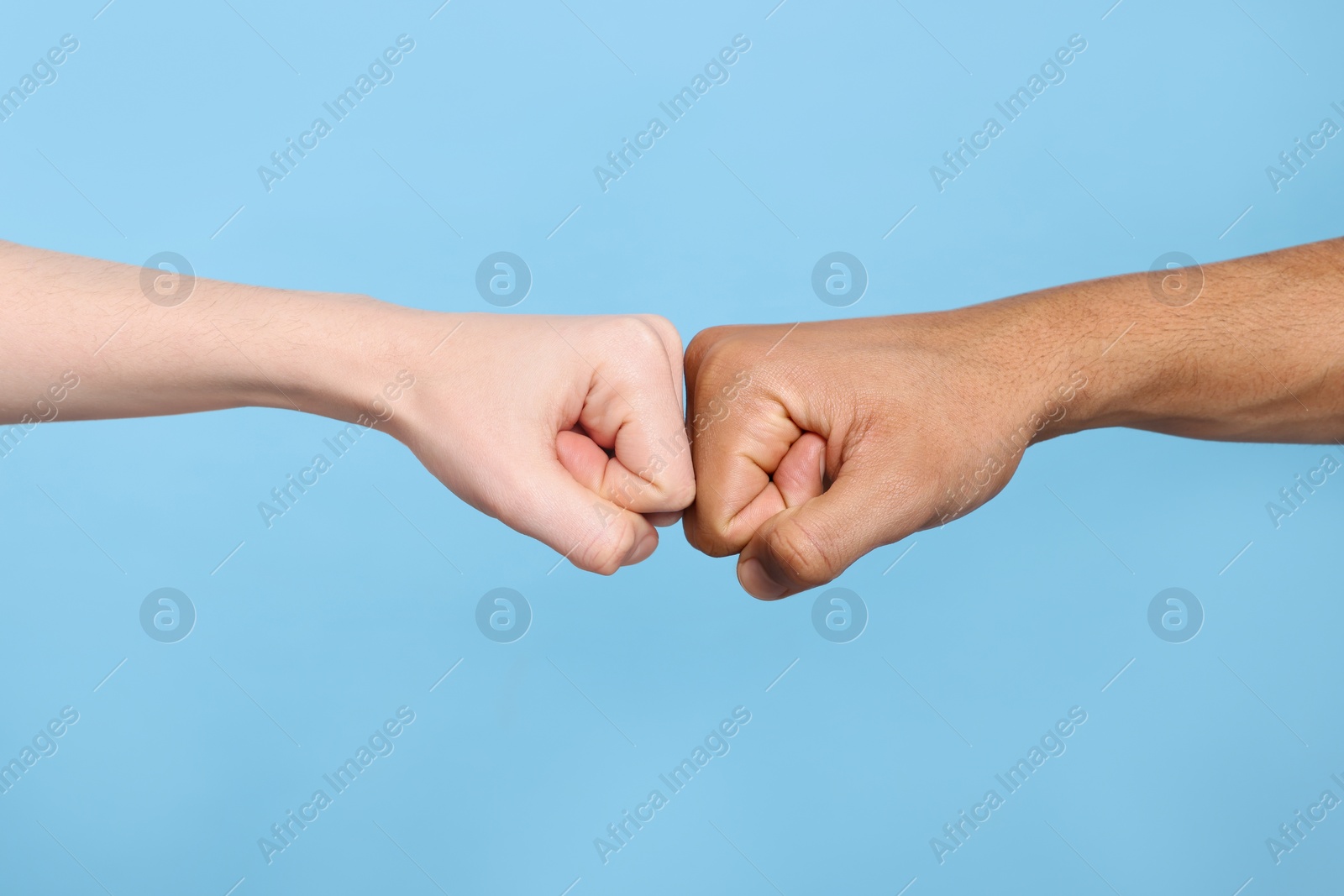 Photo of International relationships. People making fist bump on light blue background, closeup