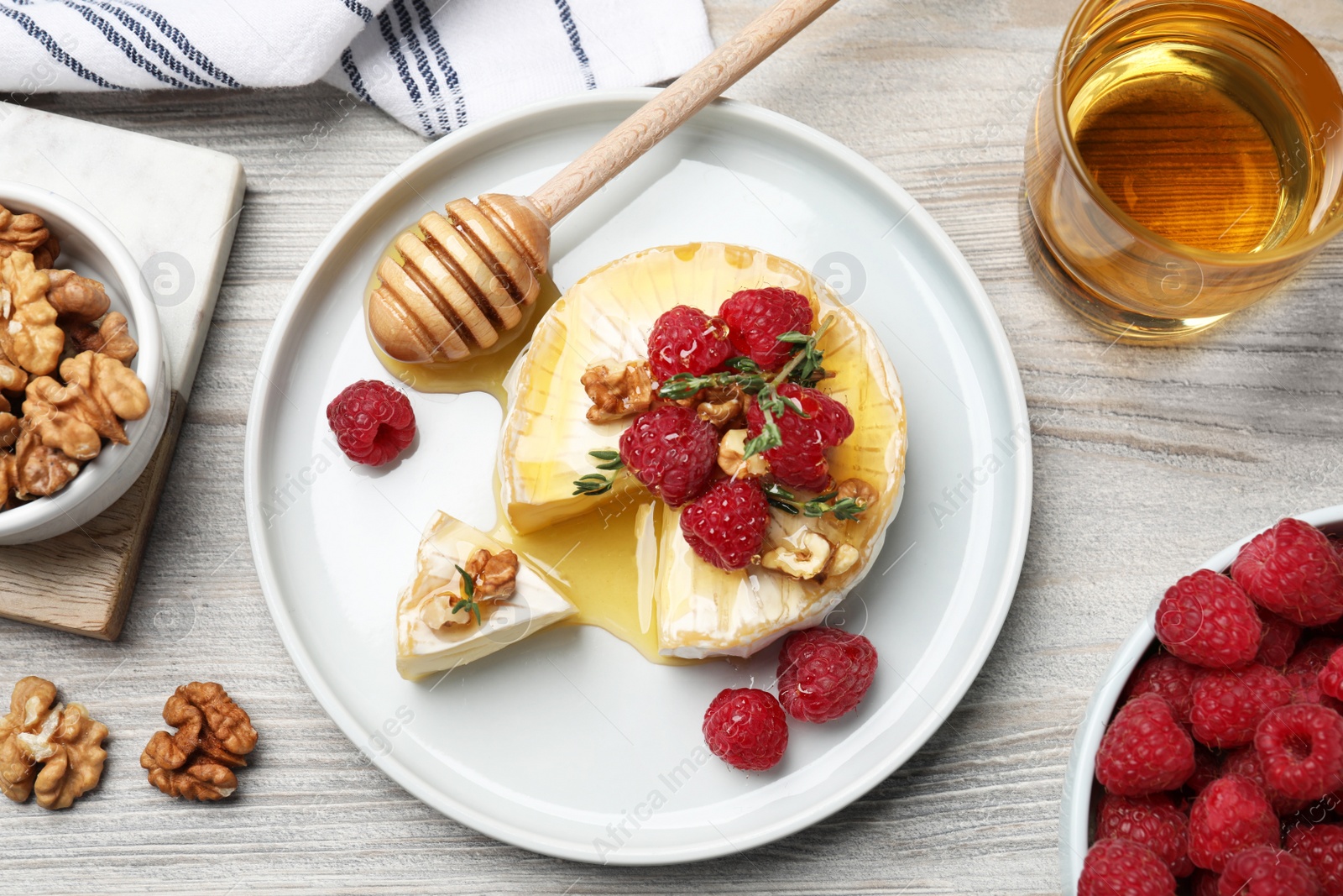 Photo of Brie cheese served with raspberries, walnuts and honey on white wooden table, flat lay