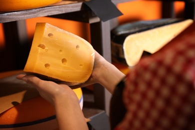 Seller with piece of delicious cheese near rack in store