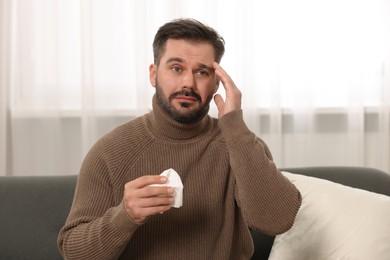 Photo of Sick man with tissue on sofa at home. Cold symptoms