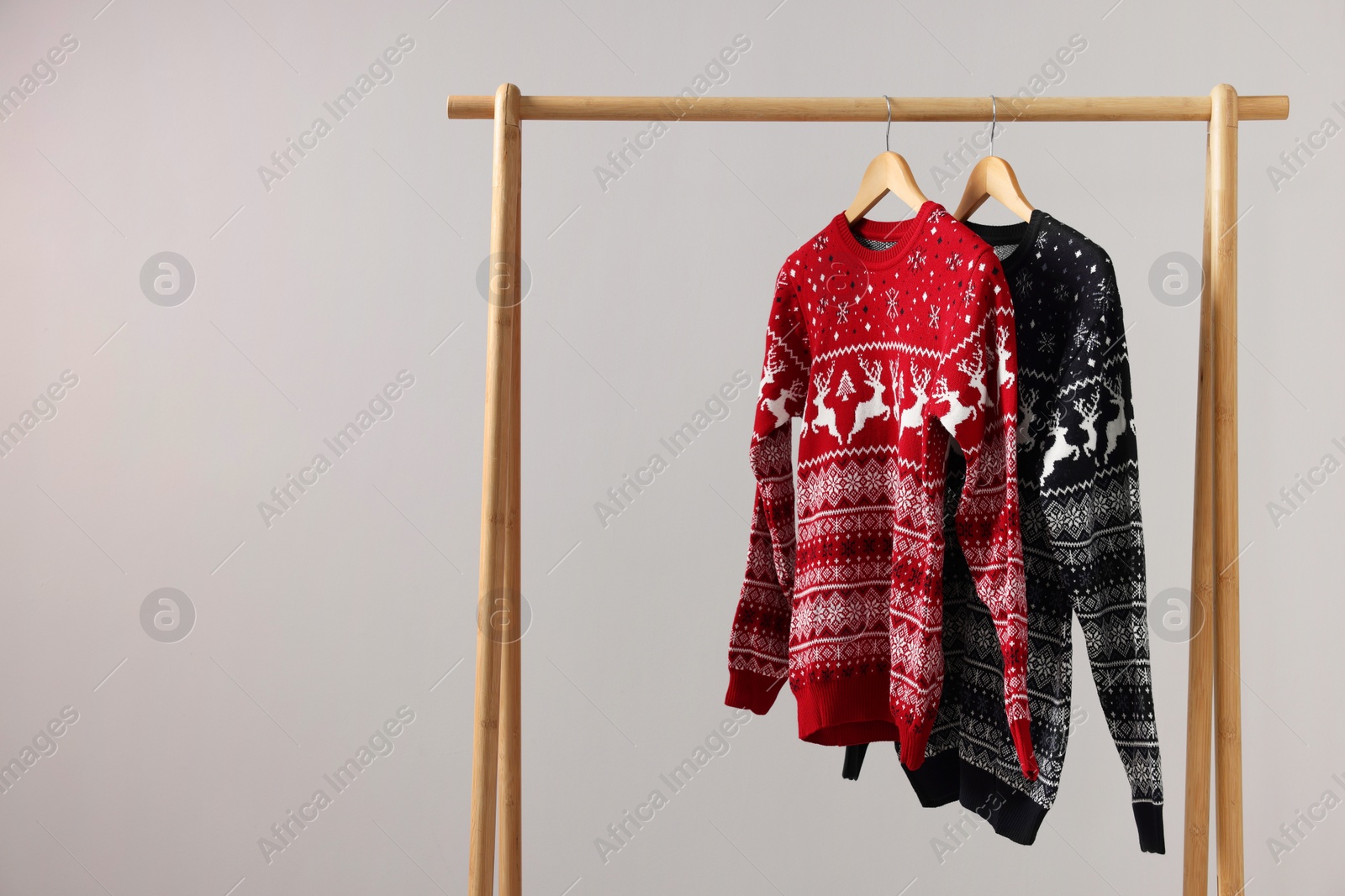 Photo of Rack with Christmas sweaters on light background, space for text