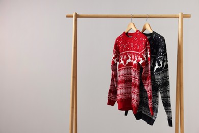 Rack with Christmas sweaters on light background, space for text